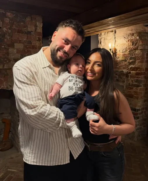 A couple holding a baby in a onesie that says, "I may be little but I am going to be a big cousin."