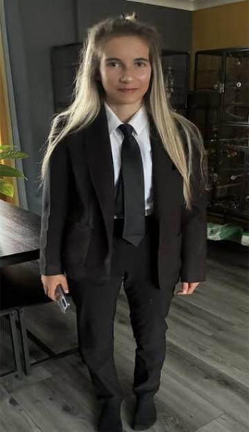 A young woman wearing a black suit and tie over a white shirt, holding a phone.