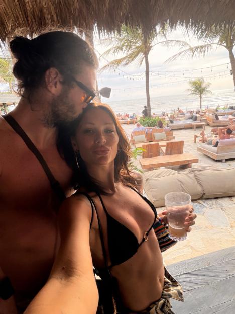 Andy Carroll and Lou Teasdale embracing outdoors near a beach.