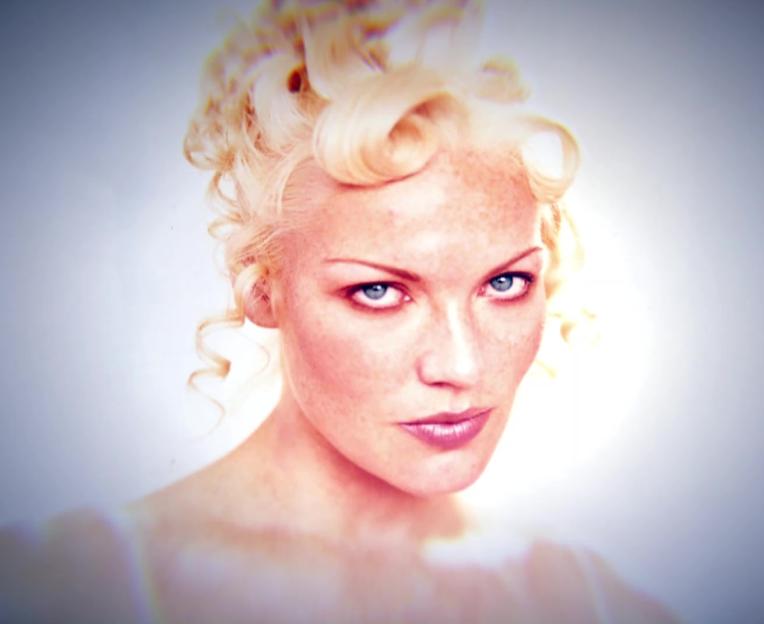 a woman with blonde hair and blue eyes looks at the camera