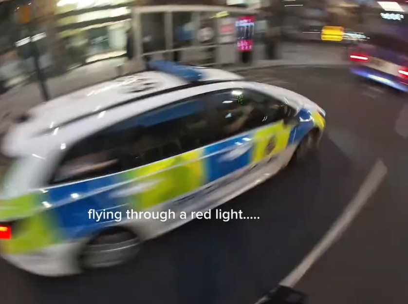 A police car, blurred from motion, "flying through a red light."