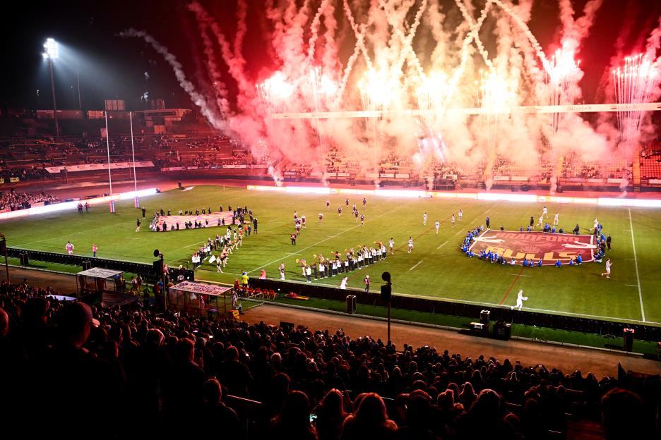 Fireworks illuminating a stadium at night, with a rugby pitch and spectators visible.