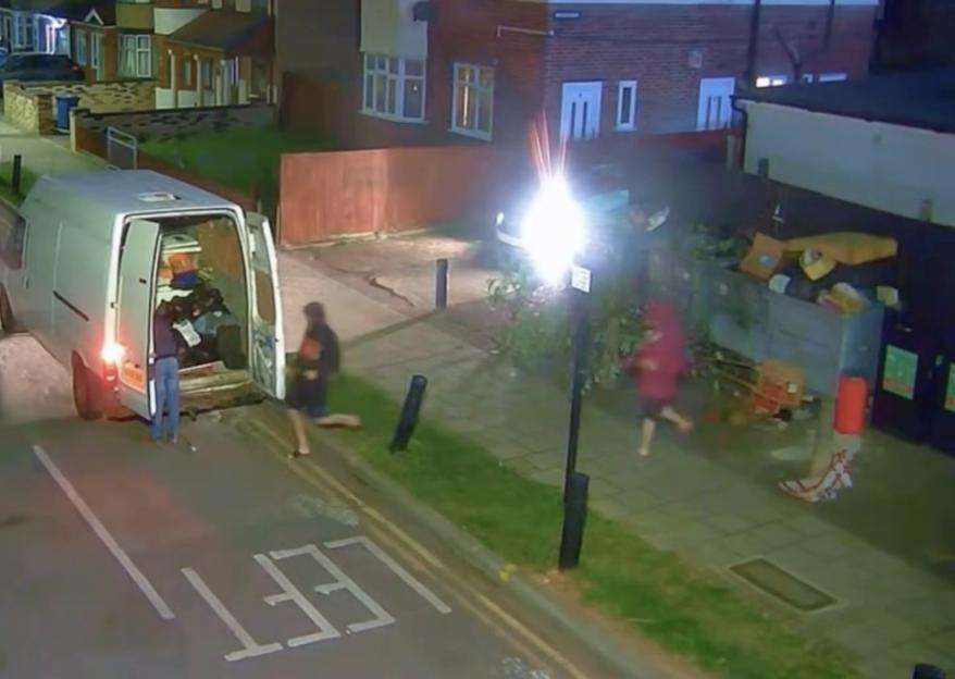 People removing items from the back of a white van onto the street at night.