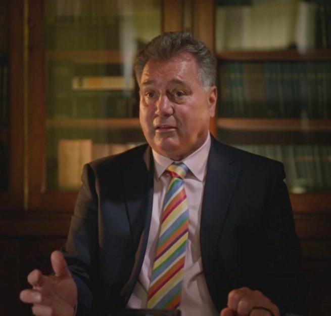 David, dressed in a suit and striped tie, gestures while speaking.