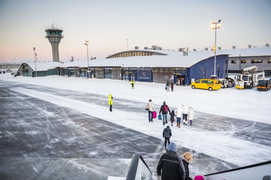 People walking on an icy airport runway in front of the snow-covered Kittila Airport terminal and control tower.
