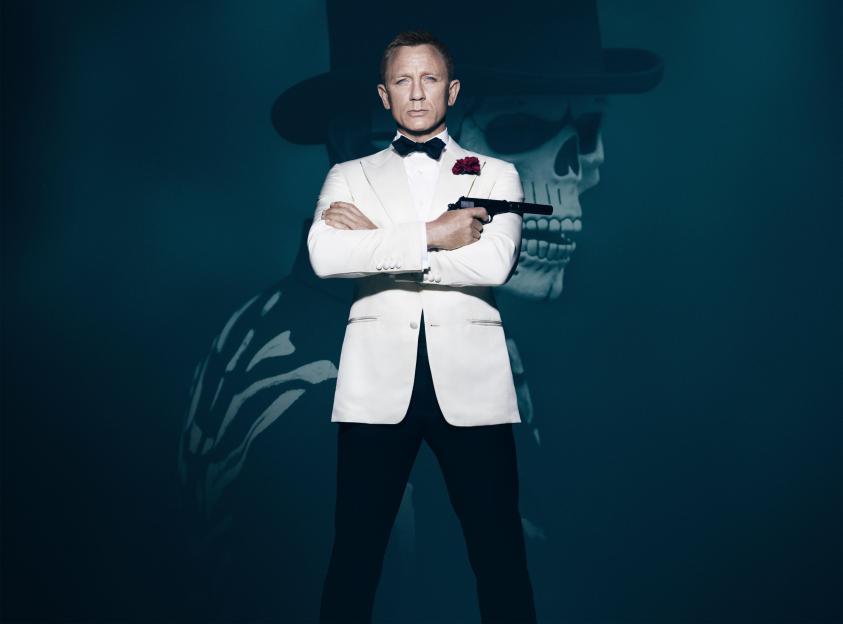 Daniel Craig as James Bond in a white tuxedo, holding a gun, with a shadowy skull in a top hat behind him.