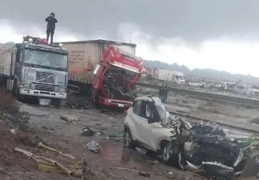 Scene of a multi-vehicle traffic accident with significant damage to a white car and a red truck, under an overcast sky.