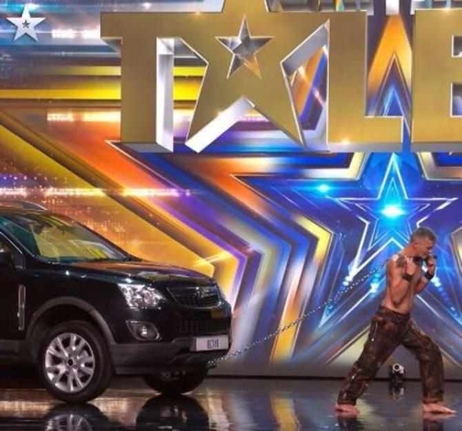 A man pulling a black car with a chain around his neck on stage.