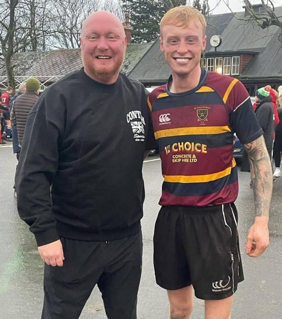 A smiling man in a black sweatshirt with a Union Jack logo next to a smiling young man in a striped rugby shirt.