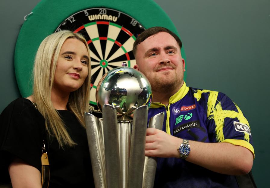 Luke Littler posing with girlfriend Faith Millar and World Darts Championship trophy.