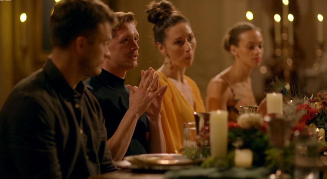 Four people sitting at a long dinner table, with candles and floral decorations.