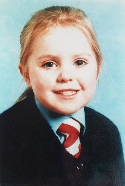 Portrait of Caroline Hogg, aged 5, smiling and wearing a blue shirt with a red and white striped tie and a dark cardigan.