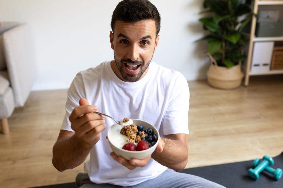 Man happily eating a bowl of yogurt, granola, and berries after a workout.