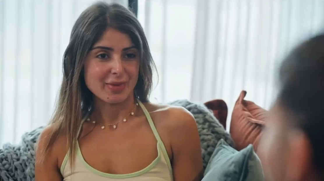 Woman with long brown hair wearing a light green top and pearl necklace.