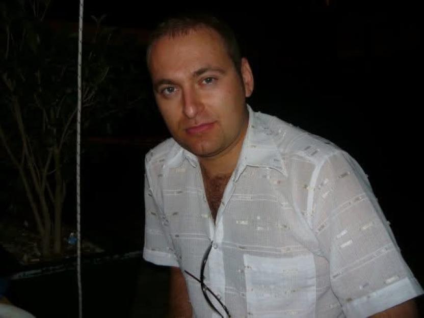 Cornel with short hair wearing a white patterned shirt.