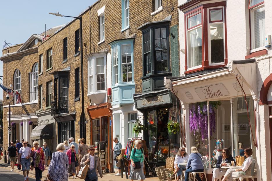 People walking and dining outside shops and restaurants on Deal High Street in Kent, England.