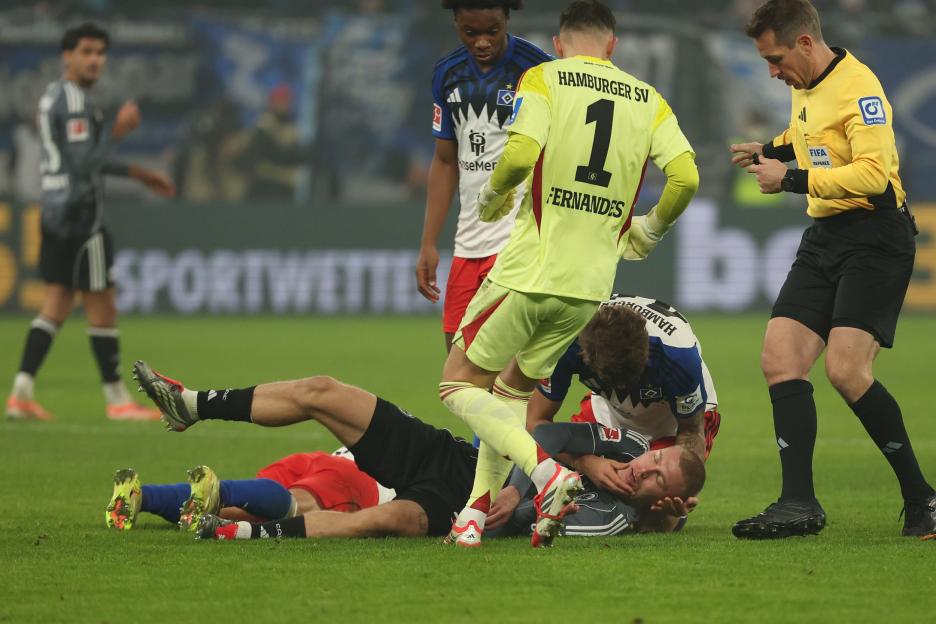 Hamburger SV's keeper Daniel Fernandes standing over an injured player on the ground while the referee looks on.