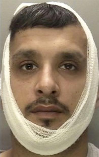 A man with dark hair, a mustache and goatee, wearing a white bandage around his chin and jaw.