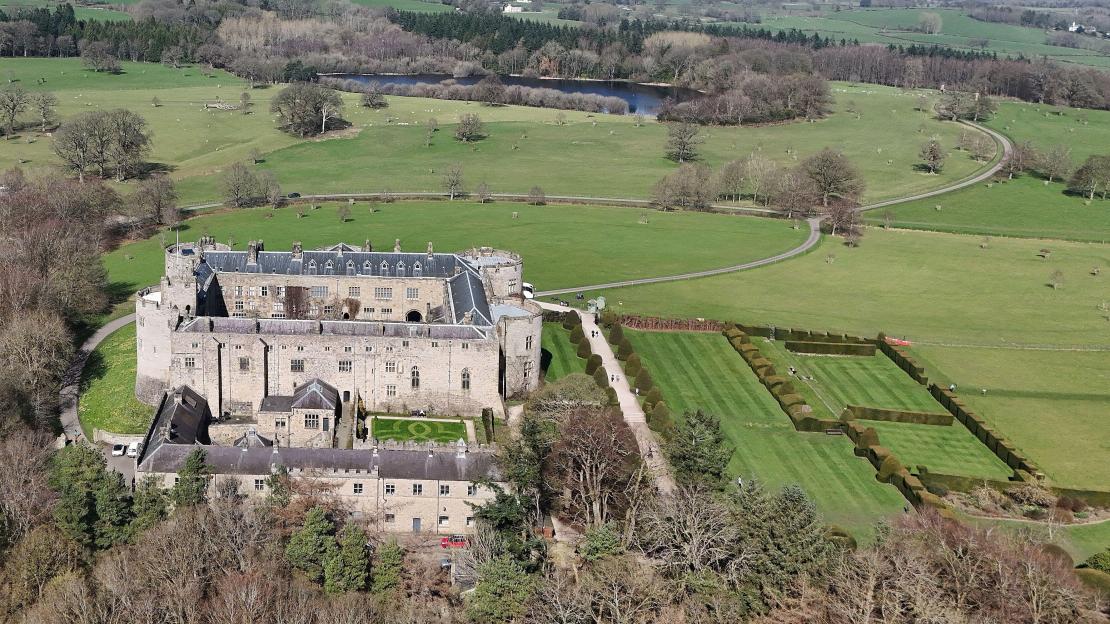 Aerial view of Chirk Castle and its gardens with surrounding fields and a lake.