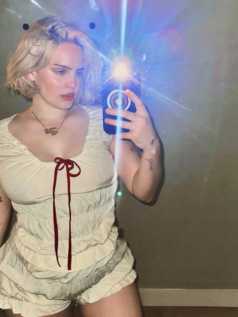 Anne Marie taking a mirror selfie in a light-colored top and shorts.