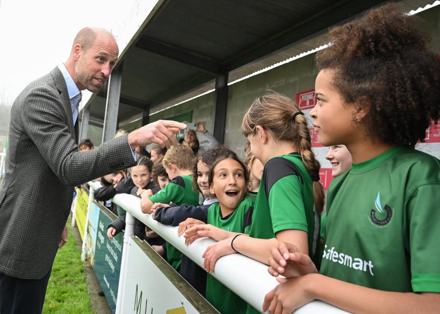 Prince William interacts with young fans wearing green jerseys at Mousehole AFC.