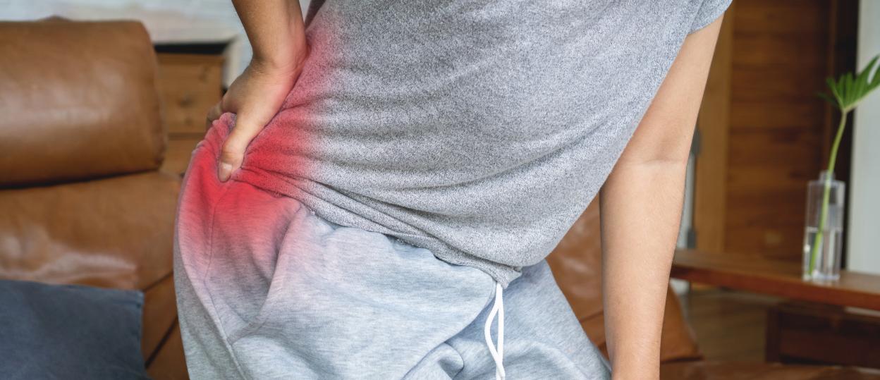 A woman in a gray shirt and sweatpants holds her knee and lower back, highlighted in red, indicating pain.