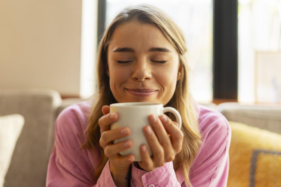 Attractive smiling woman with eyes closed holding cup of aroma coffee. Coffee break concept