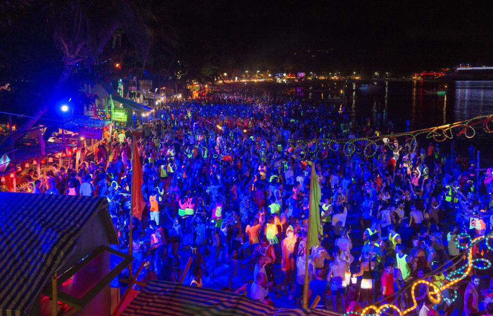 Tourists at the Full Moon party in Ko Phangan, Thailand, dancing under blacklights that make their fluorescent clothing glow.