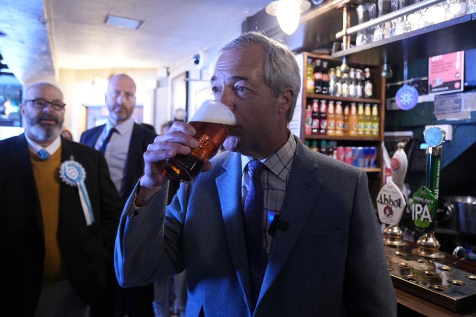 Reform UK leader Nigel Farage drinks a pint of beer at a bar.