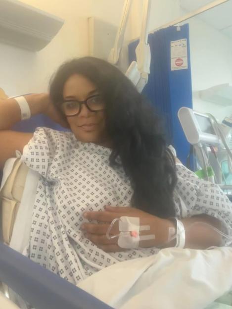 Rowetta in a hospital gown with an IV drip in her hand, looking at the camera.