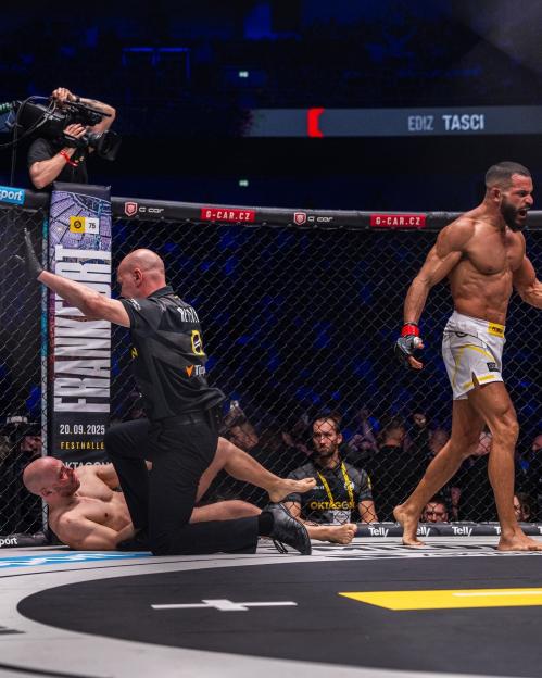 Mixed martial arts fighter Ediz Tasci stands victorious as a referee stops the fight with his opponent on the ground.
