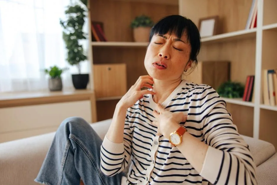 Mid Adult Japanese Woman Sitting on Sofa Scratching Her Skin at Home