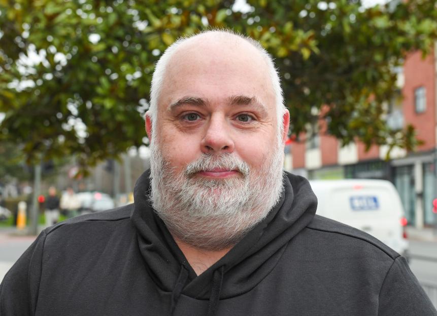 Peter Barnes, a man with a white beard and black hoodie, looks at the camera.