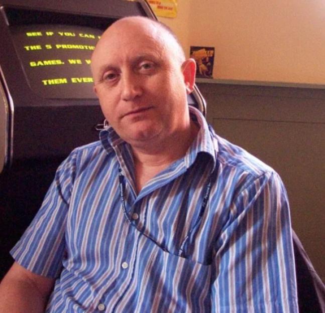 A man wearing a striped shirt sits in front of an arcade game.