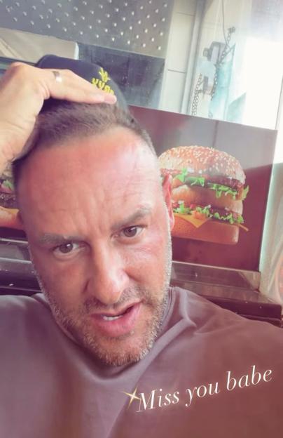Lee Andrews poses for a selfie with a burger advertisement in the background and "Miss you babe" written on the image.