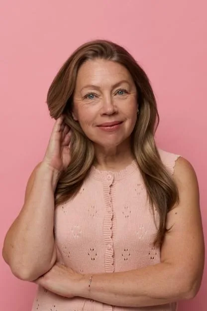Portrait of a mature woman in a pink top against a pink background.