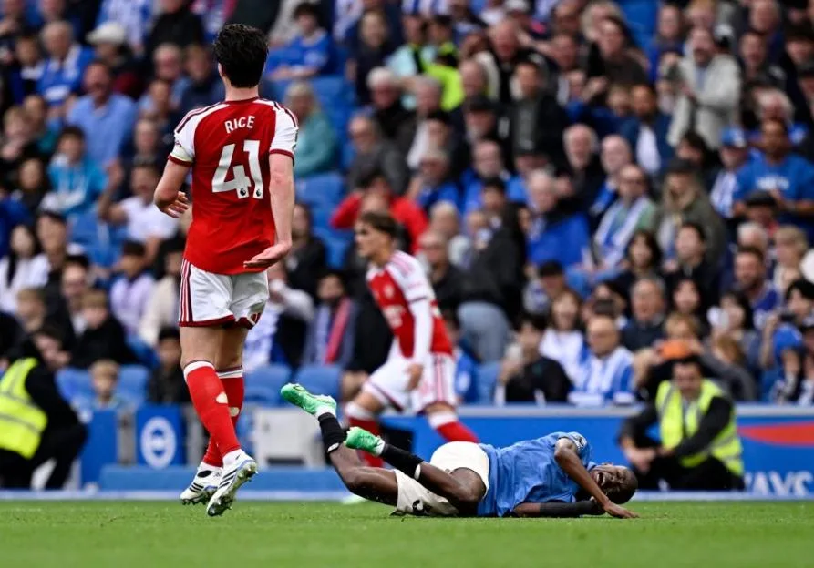 Declan Rice of Arsenal walks away from a Brighton player in blue and white on the ground, holding his leg.