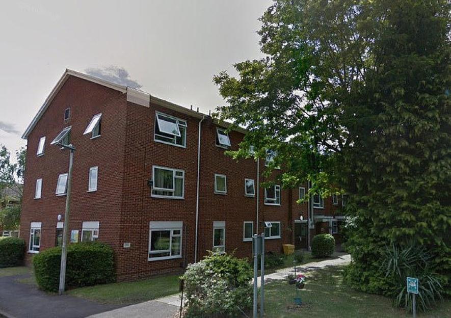 David Smith Court, a red brick apartment building with white-framed windows, surrounded by trees and bushes.