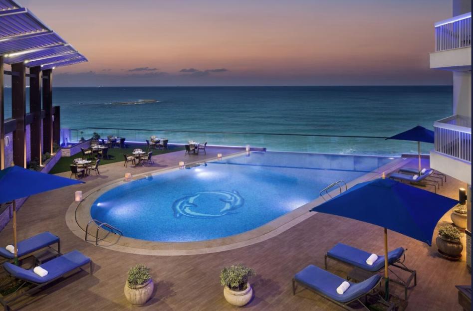 Hotel pool and outdoor dining area overlooking the ocean at sunset.