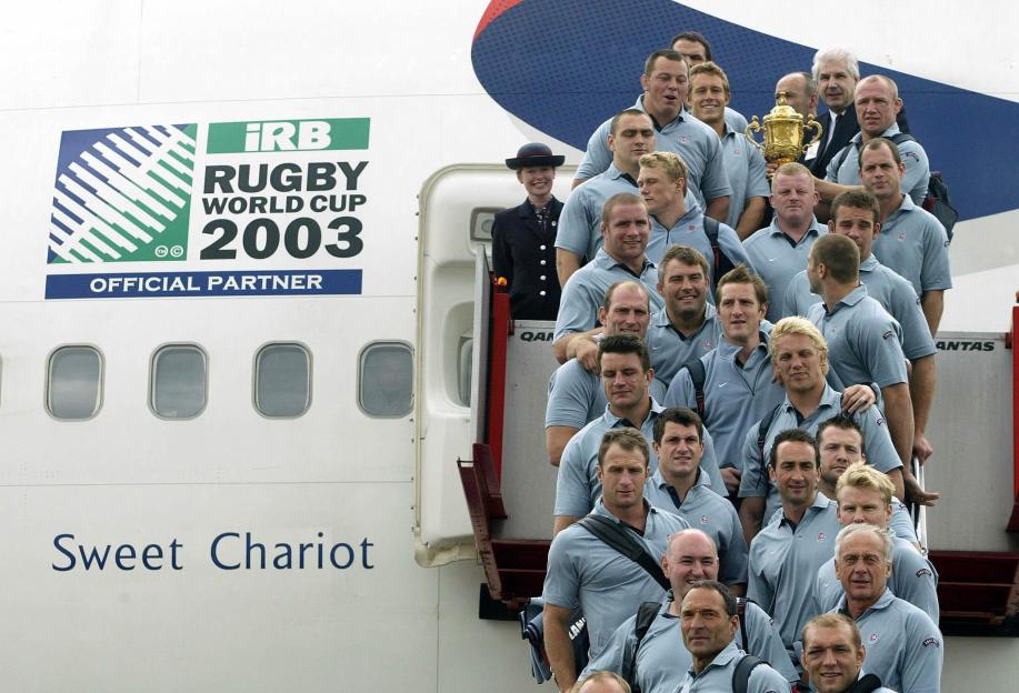 The England rugby squad with the World Cup trophy posing for a photograph on the steps of their plane, "Sweet Chariot," at Sydney Airport.