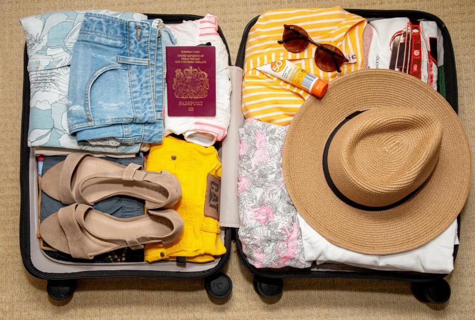 A packed suitcase with summer clothing, a passport, sunglasses, sun lotion, and a straw hat.
