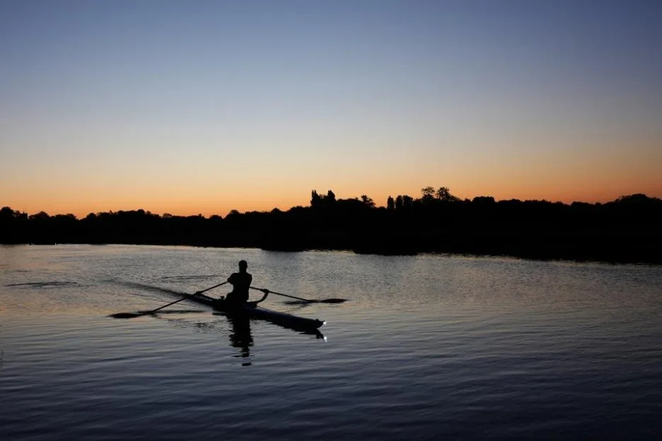 A rower trains on the River Cam at sunrise.