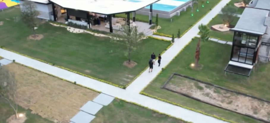 Aerial view of a modern complex with lush green lawns, walking paths, various buildings, and a swimming pool.