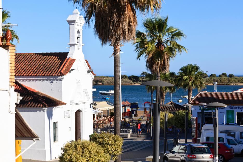White church and palm trees overlooking the sea in El Rompido, Costa de la Luz, Andalucía, Spain.