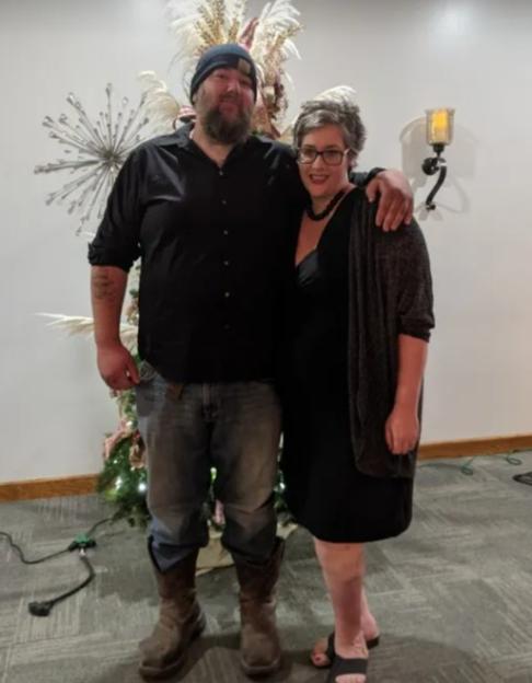 Man and woman standing together, with the man's arm around the woman.