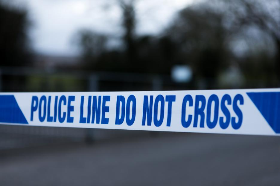 Police barrier tape in the UK that says "POLICE LINE DO NOT CROSS".