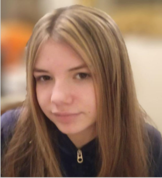 A young girl with long brown hair and highlights, wearing a navy blue zip-up jacket.