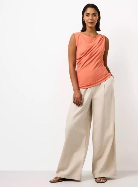 A woman models a peach top and cream wide-leg pants.