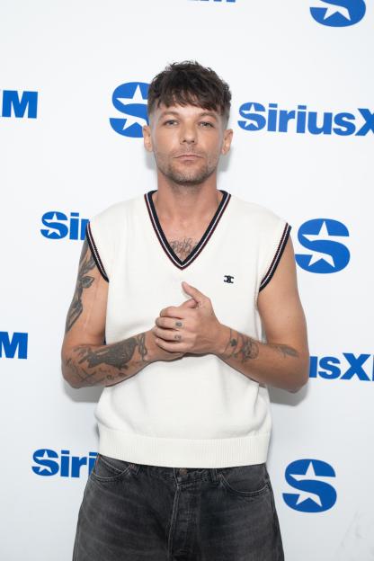Louis Tomlinson posing in a white sleeveless top against a white background with blue SiriusXM logos.