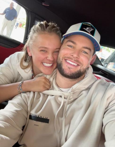 JoJo Siwa and Chris Hughes smile and pose for a selfie in a car.